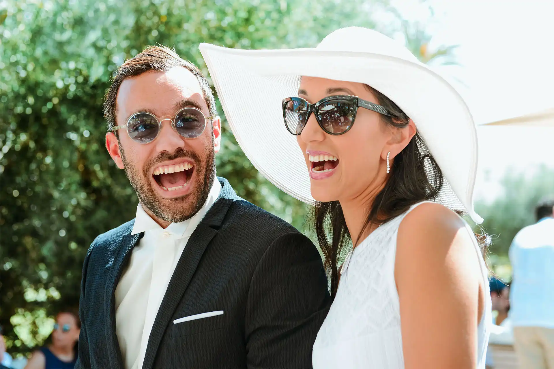 Couple élégant riant lors d’un événement en plein air, en tenue estivale chic.