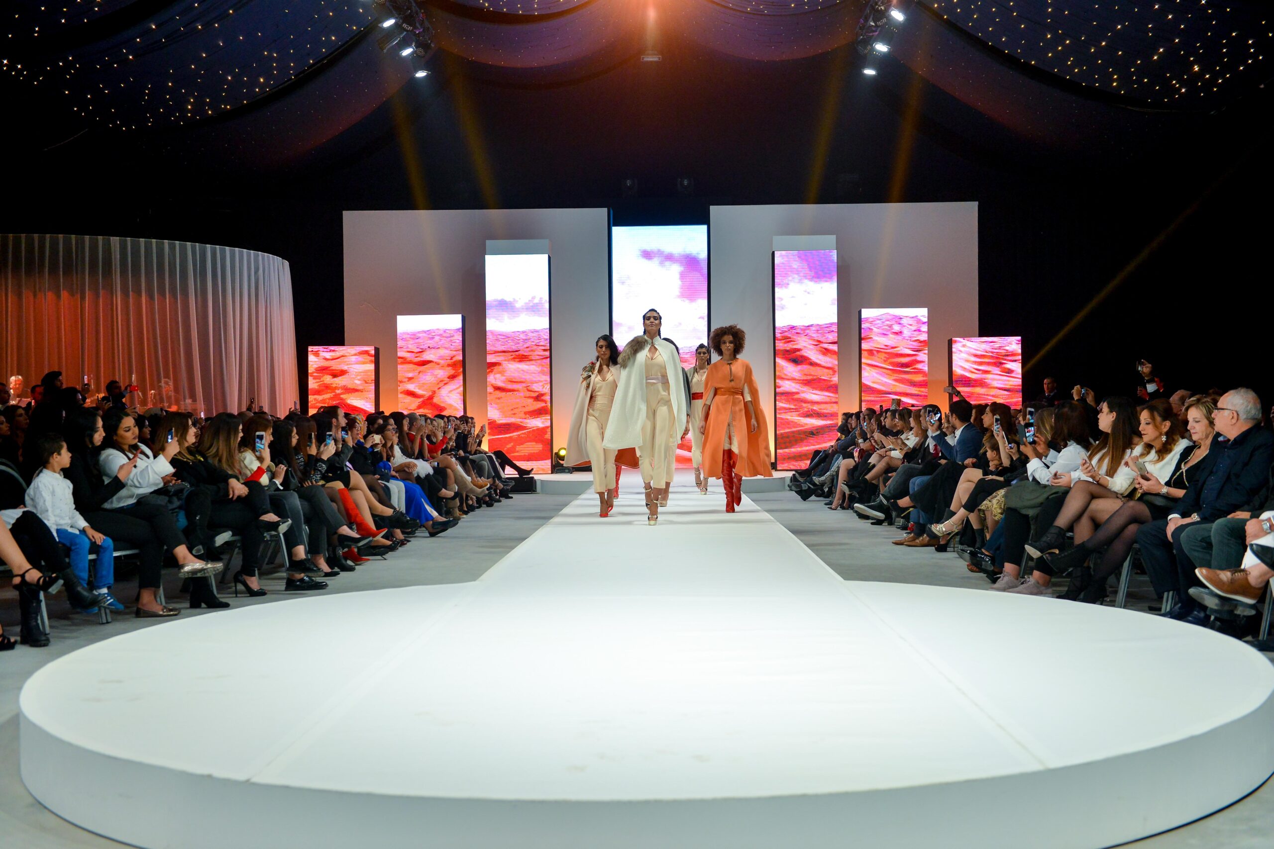 Mannequins défilant sur le podium lors du défilé de mode Laila Hadioui, avec des écrans dynamiques en arrière-plan.