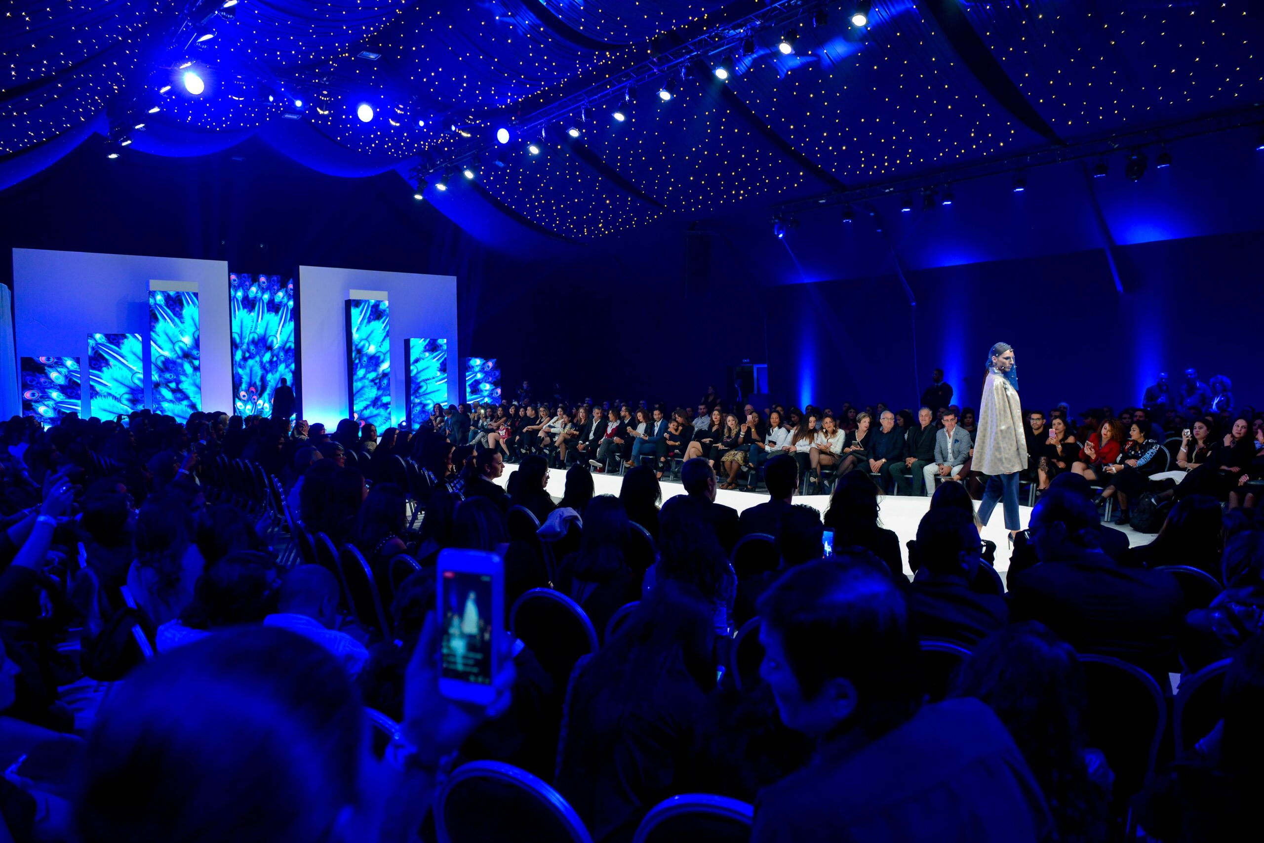 Mannequins défilant sur le podium sous des lumières bleues vives lors du défilé de mode Laila Hadioui, avec le public admirant la scène au Sofitel de Casablanca.