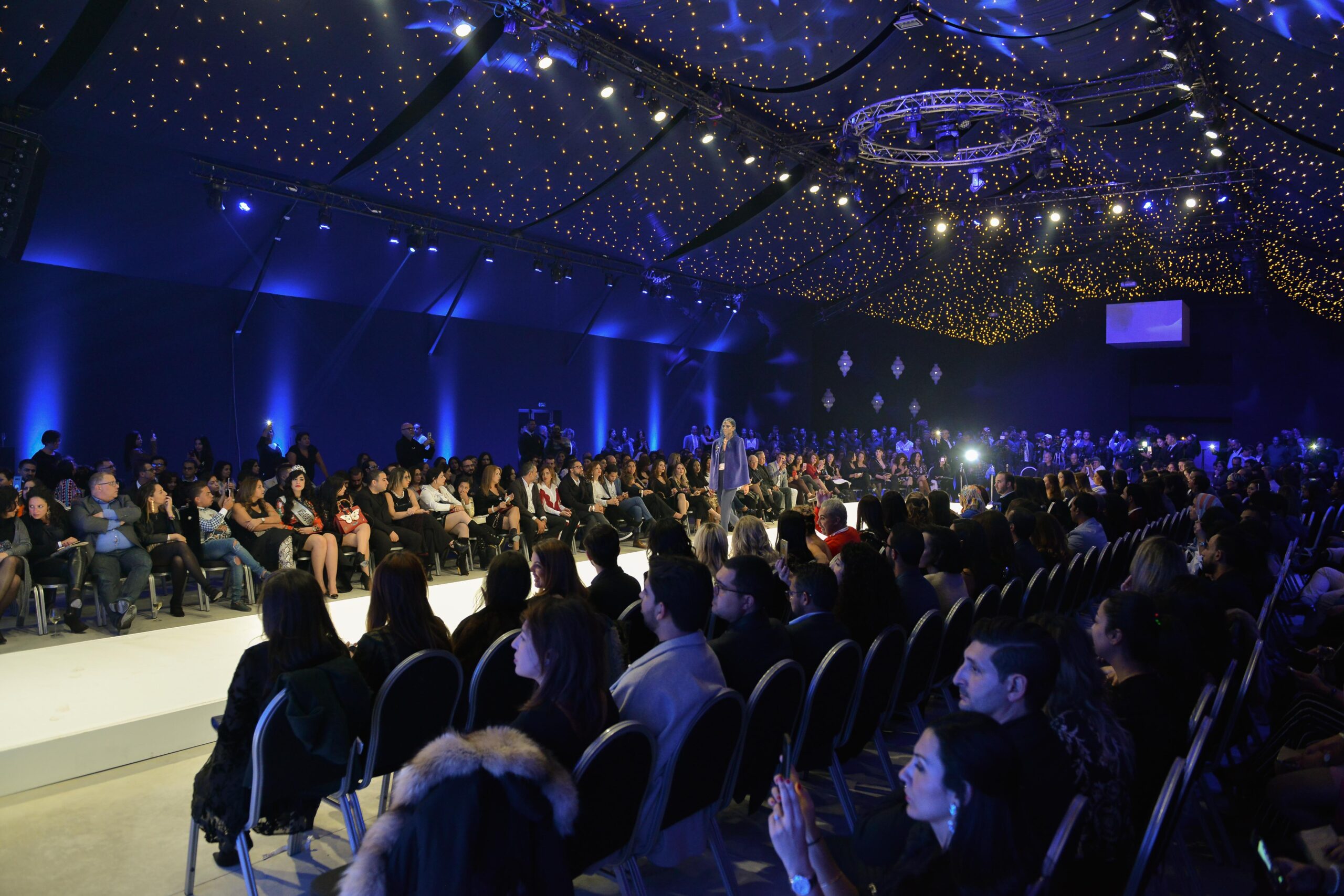 Mannequins défilant sur le podium sous des lumières bleues vives lors du défilé de mode Laila Hadioui, avec le public admirant la scène au Sofitel de Casablanca.