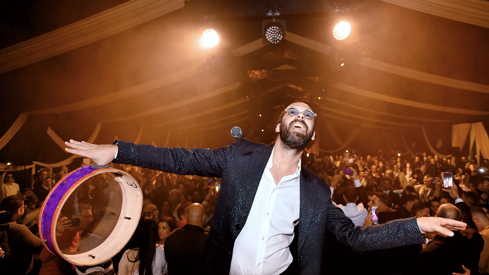 Artiste en performance sur scène, animant une foule enthousiaste lors d'un concert, avec des lumières vives et une ambiance festive.