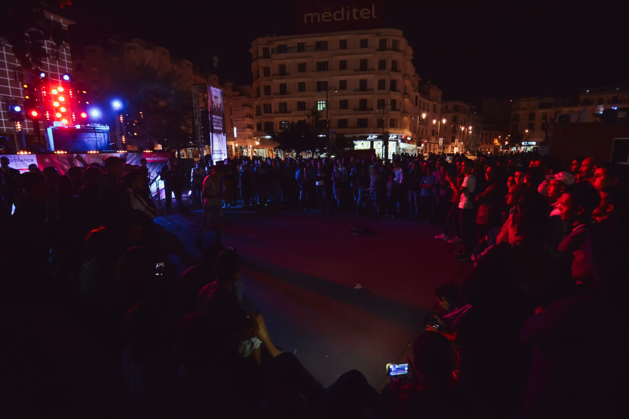 Photographie de danseur de danse urbaine en action, avec des lumières colorées illuminant la scène et un public énergique en arrière-plan.