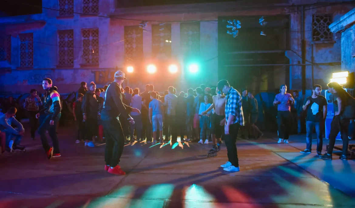 Photographie de danseur de danse urbaine en action, avec des lumières colorées illuminant la scène et un public énergique en arrière-plan.