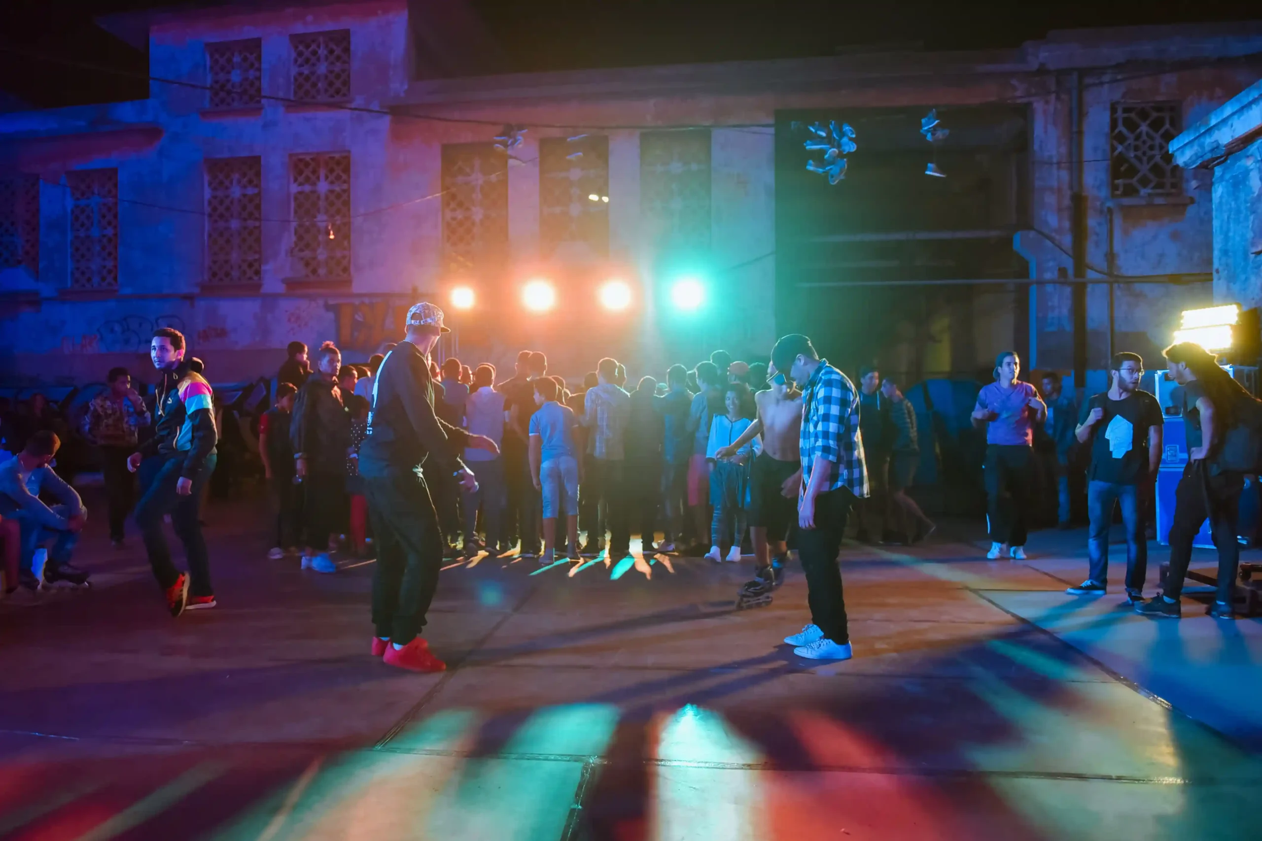 Photographie de danseur de danse urbaine en action, avec des lumières colorées illuminant la scène et un public énergique en arrière-plan.